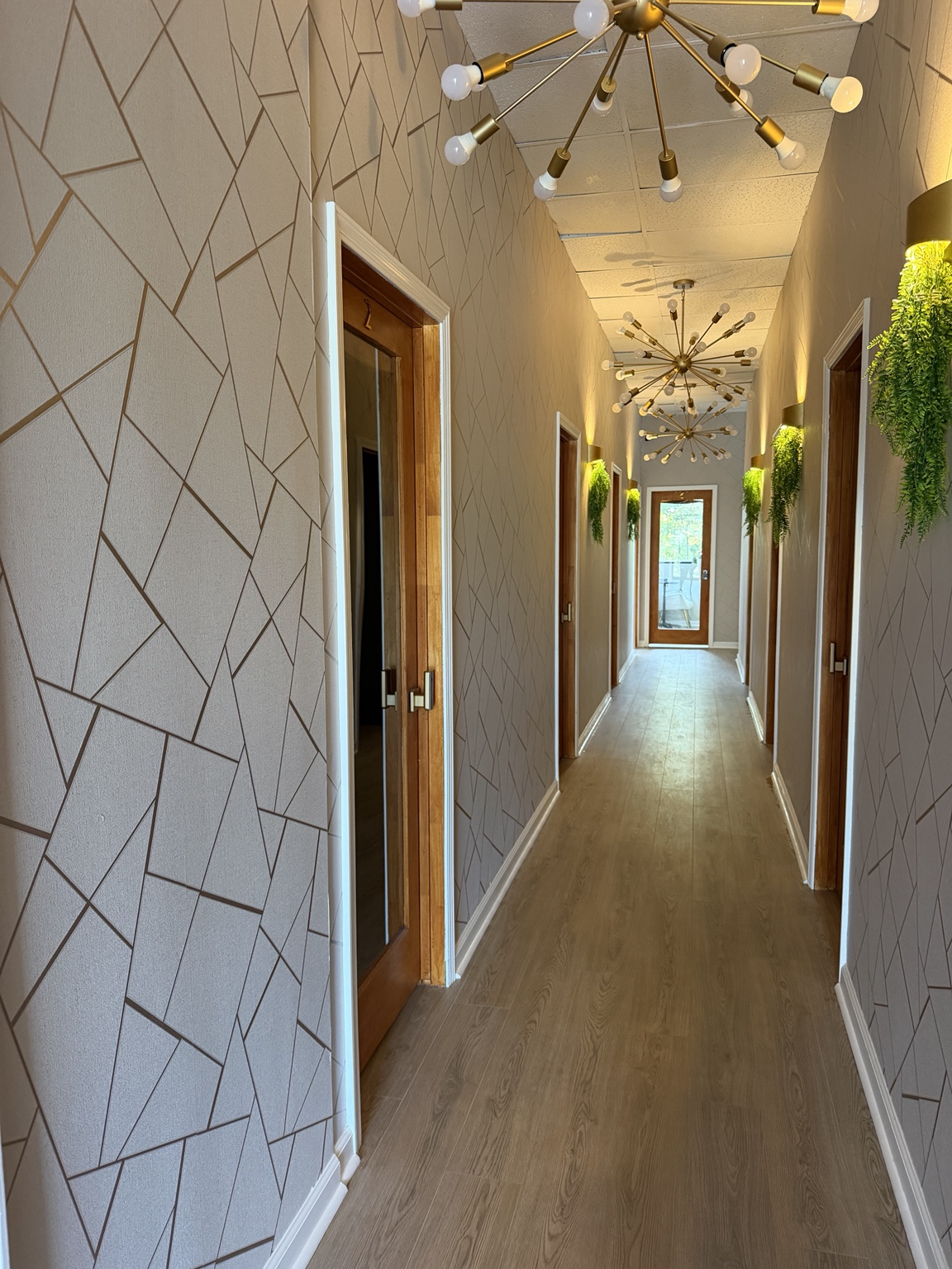 Stonecrest hallway with geometric wallpaper, gold chandeliers, and suite entrances
